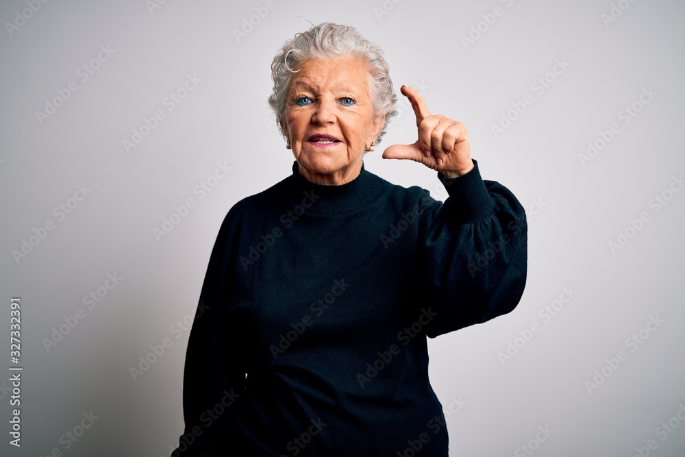 Senior beautiful woman wearing casual black sweater standing over isolated white background smiling and confident gesturing with hand doing small size sign with fingers looking and the camera. Measure