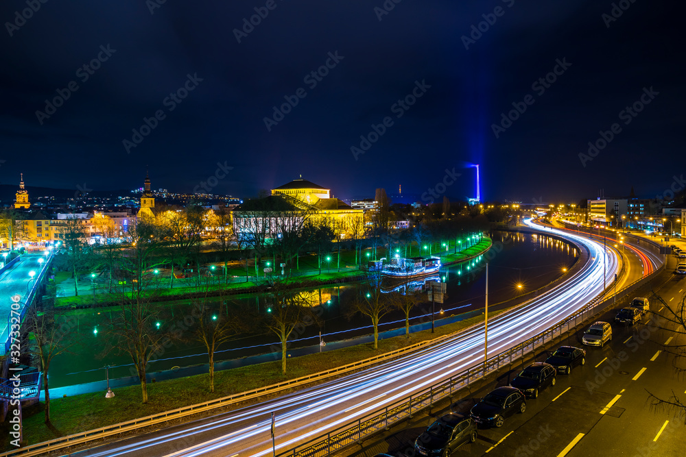 Germany, Beautiful city saarbruecken in saarland by night with lots of cars and traffic driving alongside water of saar river, illuminated in magical atmosphere