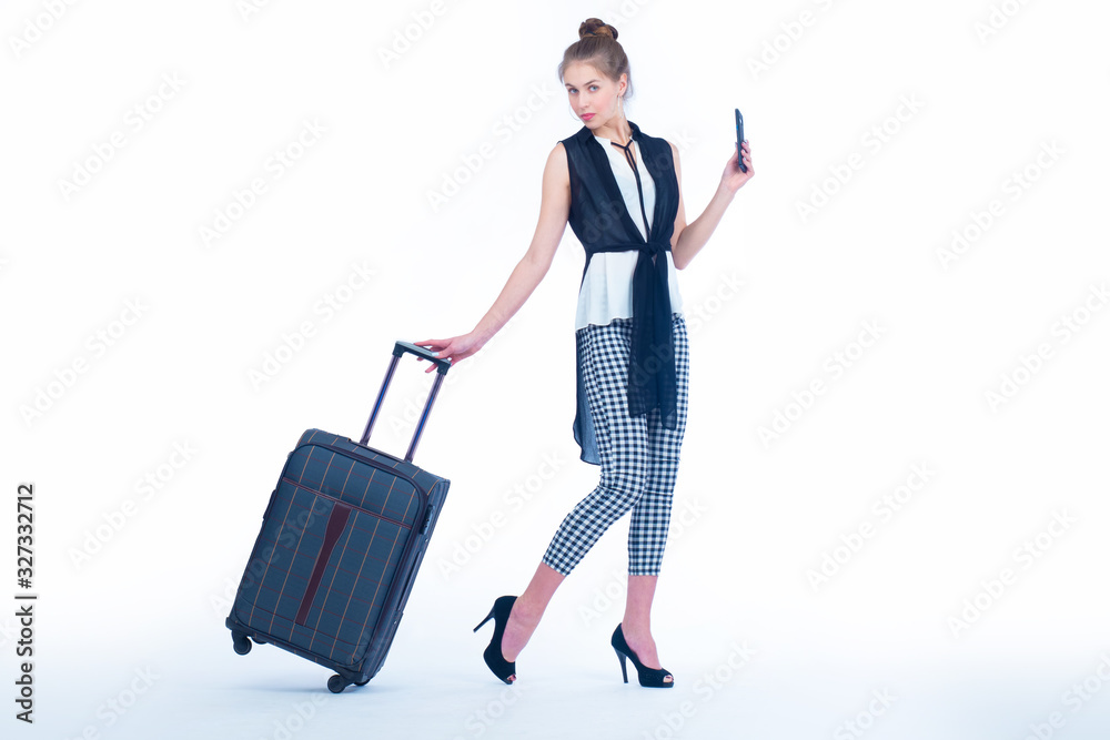 The girl demonstrates a suitcase on wheels. A woman is going on a trip. Blogging about travel. A slender girl in high-heeled shoes with a suitcase and a phone.