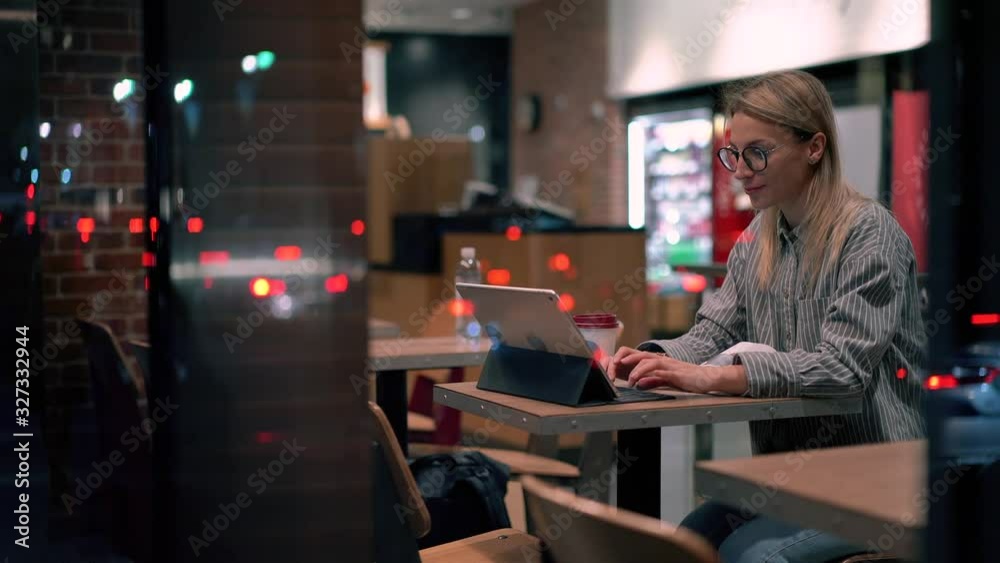 Female remote worker in casual wear and optical glasses working on design for website using public internet connection on digital tablet, Caucasian woman with coffee to go doing distance work indoors