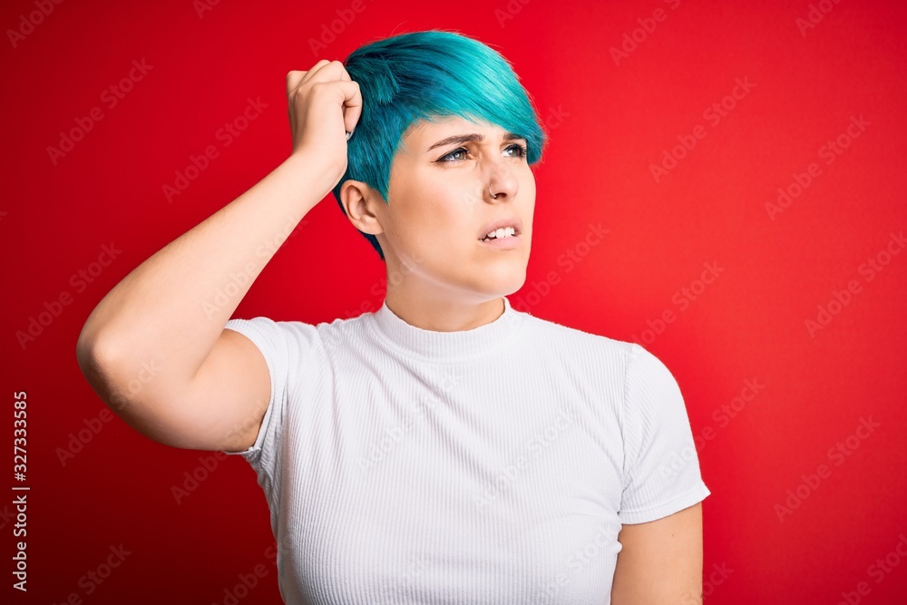 Young beautiful woman with blue fashion hair wearing casual t-shirt over red background confuse and wondering about question. Uncertain with doubt, thinking with hand on head. Pensive concept. Young beautiful woman with blue fashion hair wearing casual t-shirt over red background confuse and wondering about question. Uncertain with doubt, thinking with hand on head. Pensive concept.