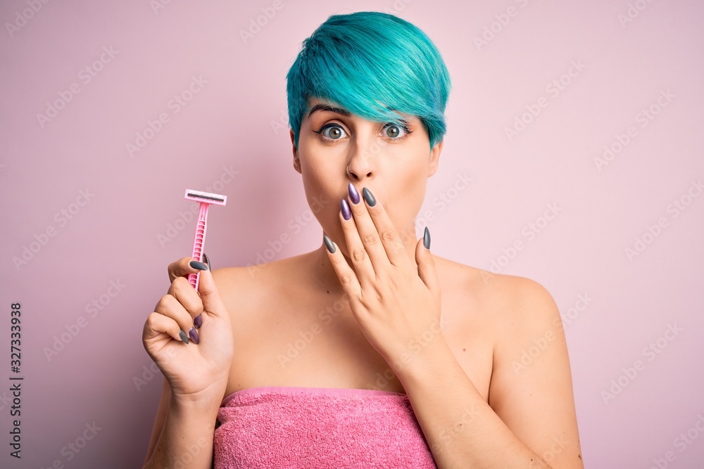 Obraz premium Young woman with blue fashion hair wearing pink towel holding beauty care razor cover mouth with hand shocked with shame for mistake, expression of fear, scared in silence, secret concept
