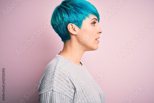 Young beautiful woman with blue fashion hair wearing casual sweater over pink background looking to side, relax profile pose with natural face with confident smile. © Krakenimages.com