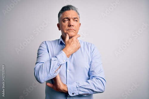 Middle age handsome grey-haired business man wearing elegant shirt over white background with hand on chin thinking about question, pensive expression. Smiling with thoughtful face. Doubt concept.