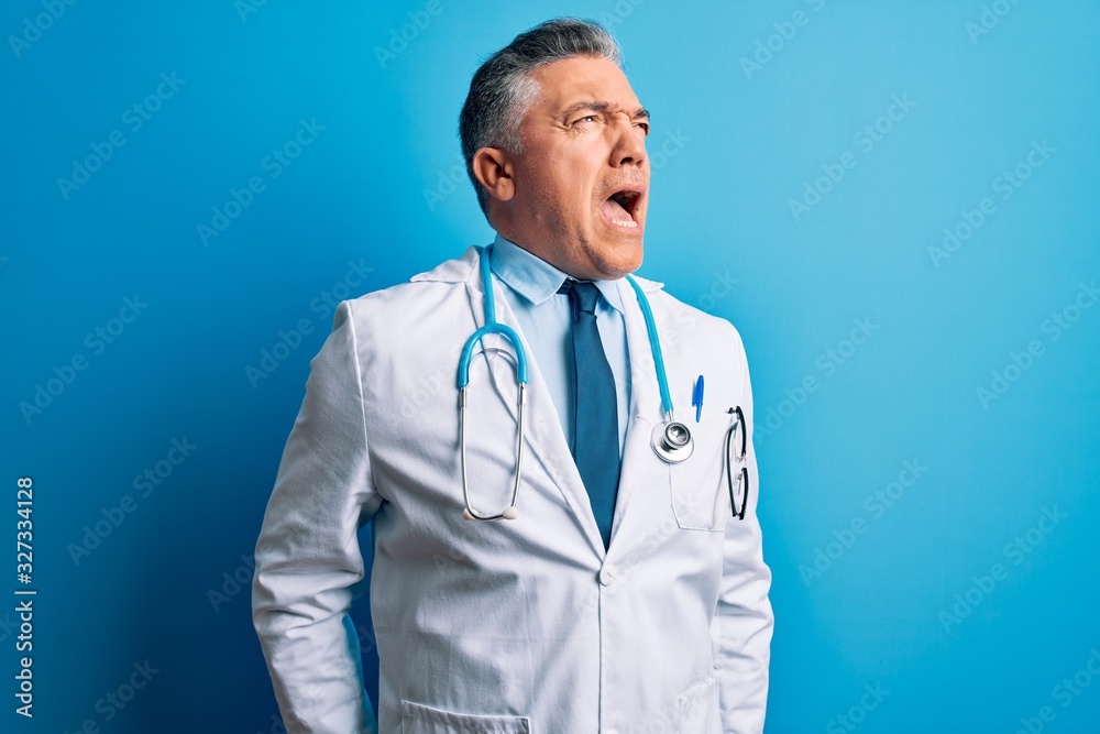 Middle age handsome grey-haired doctor man wearing coat and blue stethoscope angry and mad screaming frustrated and furious, shouting with anger. Rage and aggressive concept. Middle age handsome grey-haired doctor man wearing coat and blue stethoscope angry and mad screaming frustrated and furious, shouting with anger. Rage and aggressive concept.