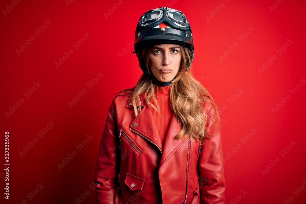Young beautiful brunette motrocyclist woman wearing moto helmet over red background depressed and worry for distress, crying angry and afraid. Sad expression.