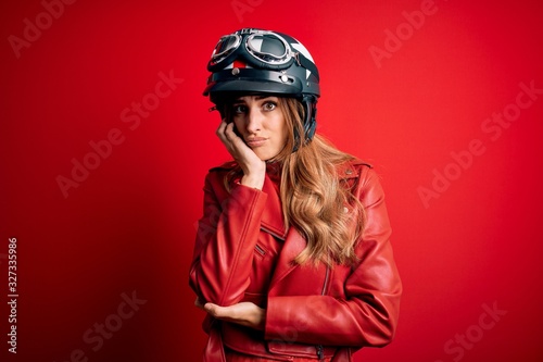 Young beautiful brunette motrocyclist woman wearing moto helmet over red background thinking looking tired and bored with depression problems with crossed arms.