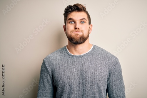 Young handsome blond man with beard and blue eyes wearing casual sweater puffing cheeks with funny face. Mouth inflated with air, crazy expression. © Krakenimages.com
