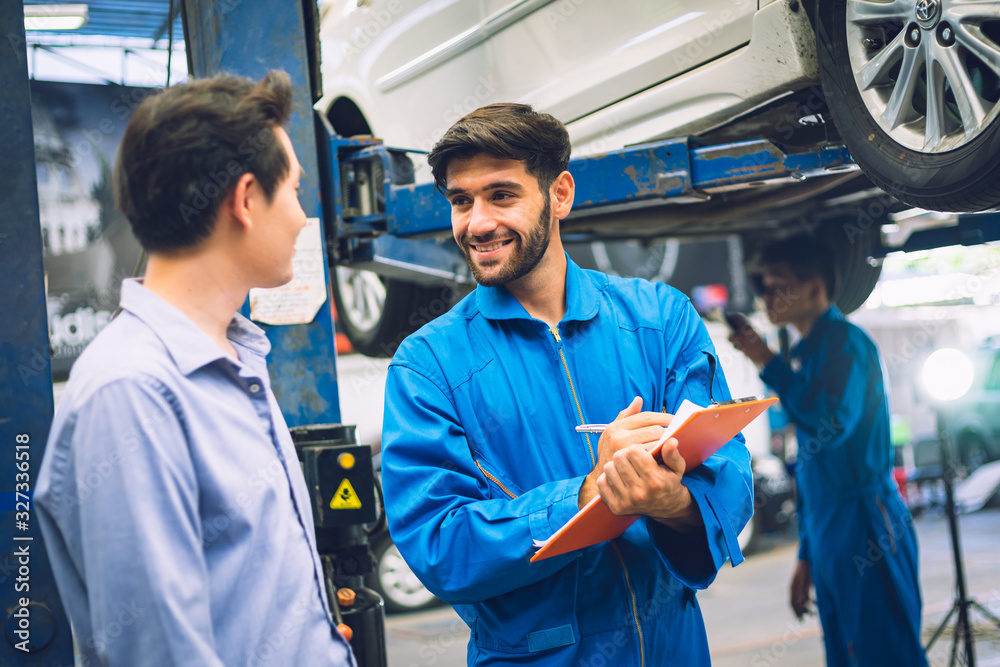 Mechanic holding clipboard with car owner in the workshop garage. Car auto services concepts Mechanic holding clipboard with car owner in the workshop garage. Car auto services concepts