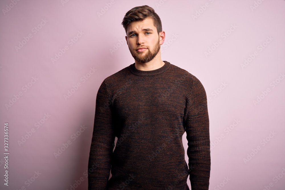 Fototapeta premium Young blond man with beard and blue eyes wearing casual sweater over pink background Relaxed with serious expression on face. Simple and natural looking at the camera.