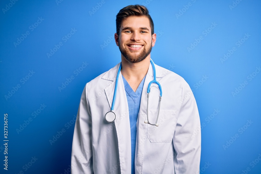Young blond doctor man with beard and blue eyes wearing white coat and stethoscope with a happy and cool smile on face. Lucky person. Young blond doctor man with beard and blue eyes wearing white coat and stethoscope with a happy and cool smile on face. Lucky person.