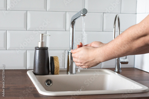 Hand washing underwater from a faucet in the kitchen. leanliness, water saving, washing dishes in a bright Scandinavian interior