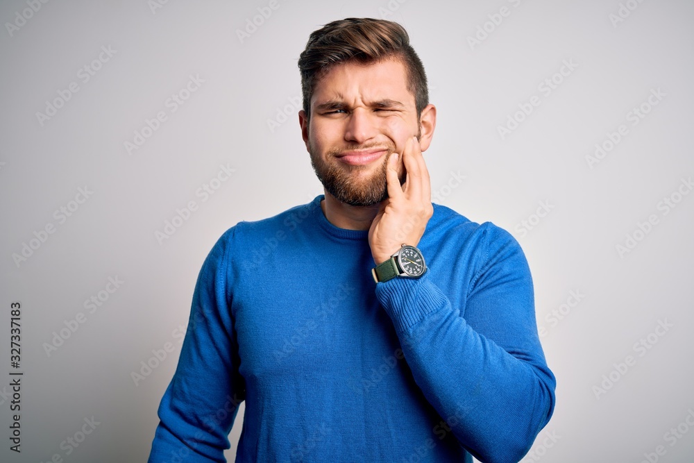 Young handsome blond man with beard and blue eyes wearing casual sweater touching mouth with hand with painful expression because of toothache or dental illness on teeth. Dentist Young handsome blond man with beard and blue eyes wearing casual sweater touching mouth with hand with painful expression because of toothache or dental illness on teeth. Dentist