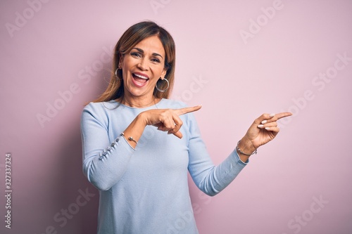 Middle age beautiful woman wearing casual t-shirt standing over isolated pink background smiling and looking at the camera pointing with two hands and fingers to the side.