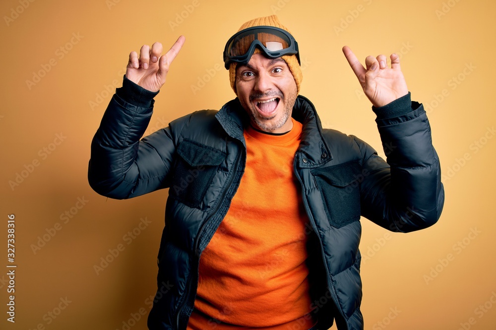Young handsome skier man skiing wearing snow sportswear using ski goggles smiling amazed and surprised and pointing up with fingers and raised arms. Young handsome skier man skiing wearing snow sportswear using ski goggles smiling amazed and surprised and pointing up with fingers and raised arms.