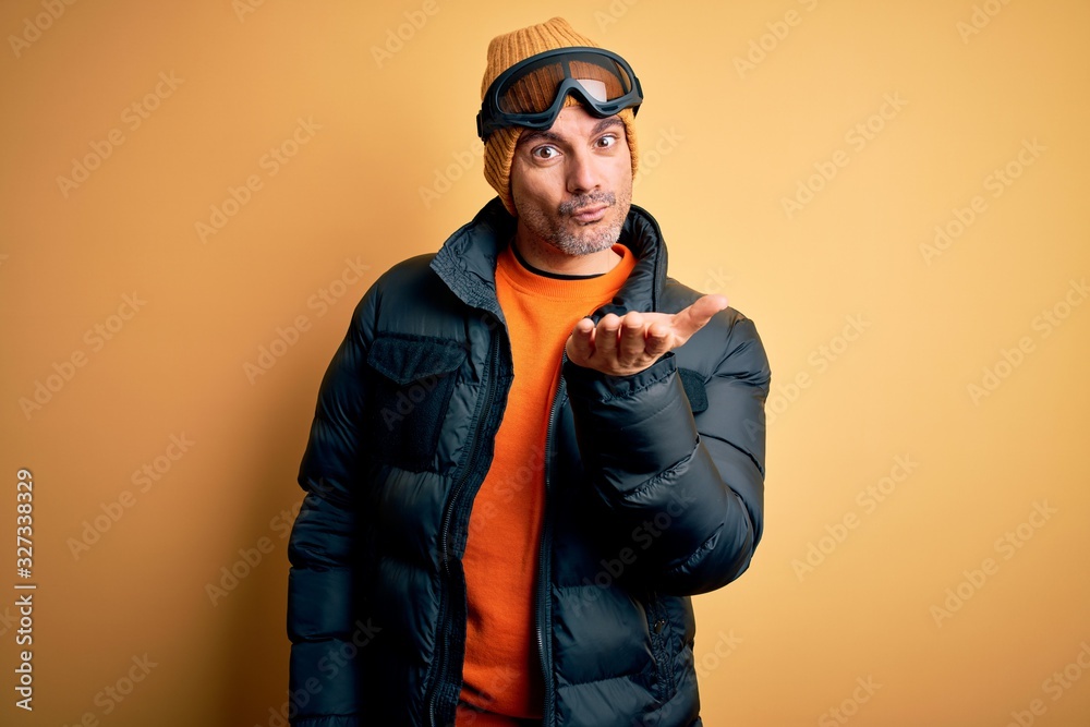 Young handsome skier man skiing wearing snow sportswear using ski goggles looking at the camera blowing a kiss with hand on air being lovely and sexy. Love expression. Young handsome skier man skiing wearing snow sportswear using ski goggles looking at the camera blowing a kiss with hand on air being lovely and sexy. Love expression.