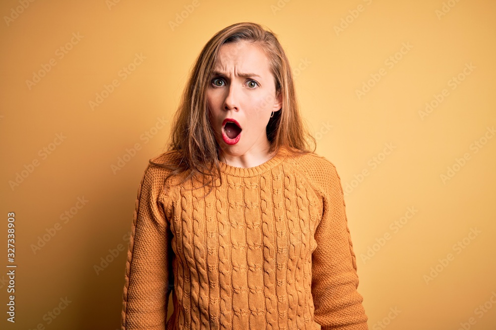 Young beautiful blonde woman wearing casual sweater standing over yellow background In shock face, looking skeptical and sarcastic, surprised with open mouth Young beautiful blonde woman wearing casual sweater standing over yellow background In shock face, looking skeptical and sarcastic, surprised with open mouth