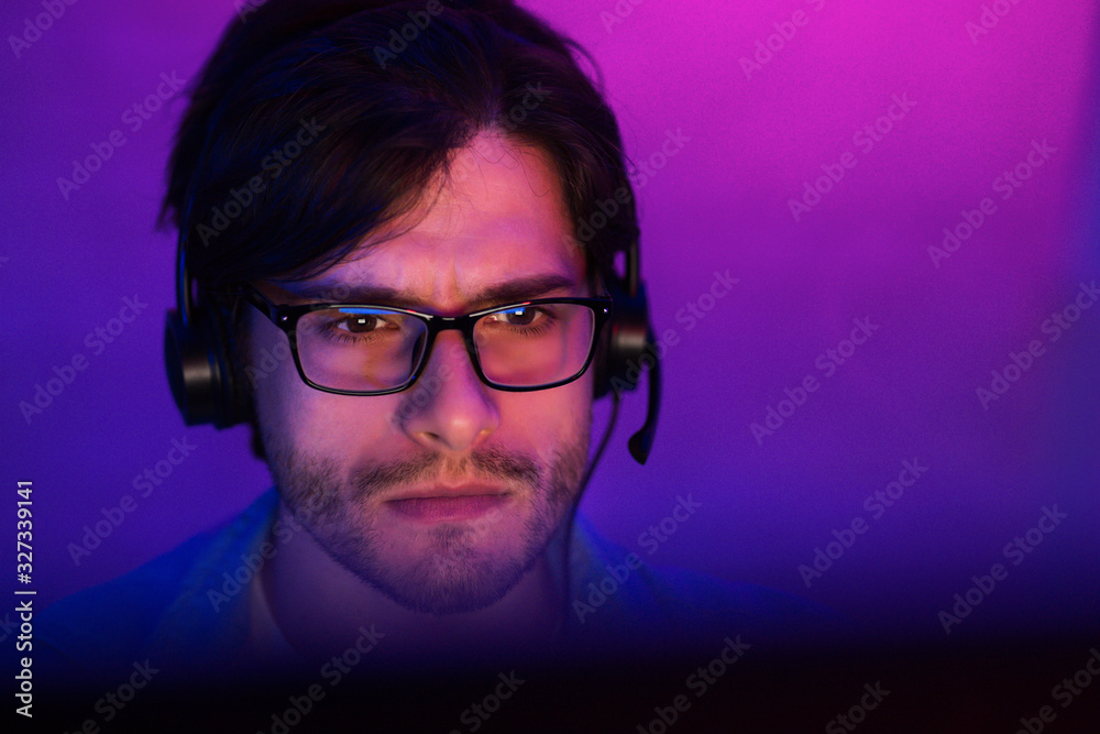 Millennial Guy Playing Online Videogame Sitting At Home, Neon Lights Millennial Guy Playing Online Videogame Sitting At Home, Neon Lights