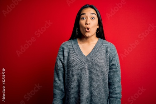 Young beautiful asian woman wearing casual sweater standing over isolated red background afraid and shocked with surprise expression, fear and excited face. © Krakenimages.com