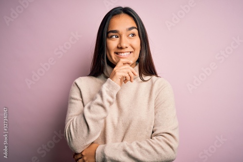 Young beautiful asian woman wearing casual turtleneck sweater over pink background with hand on chin thinking about question, pensive expression. Smiling with thoughtful face. Doubt concept.