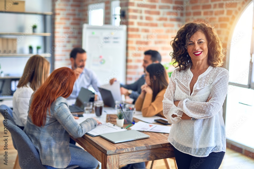 Group of business workers working together. Middle age beautiful businesswoman standing smiling happy looking at the camera at the office Group of business workers working together. Middle age beautiful businesswoman standing smiling happy looking at the camera at the office