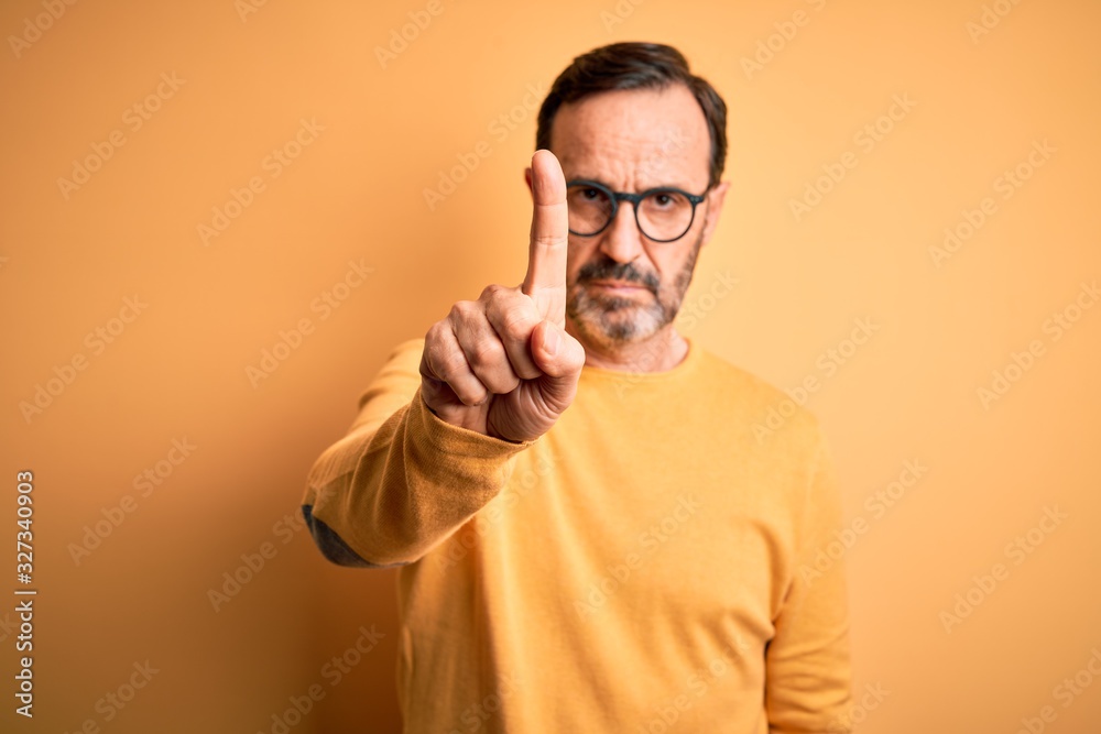 Middle age hoary man wearing casual sweater and glasses over isolated yellow background Pointing with finger up and angry expression, showing no gesture Middle age hoary man wearing casual sweater and glasses over isolated yellow background Pointing with finger up and angry expression, showing no gesture