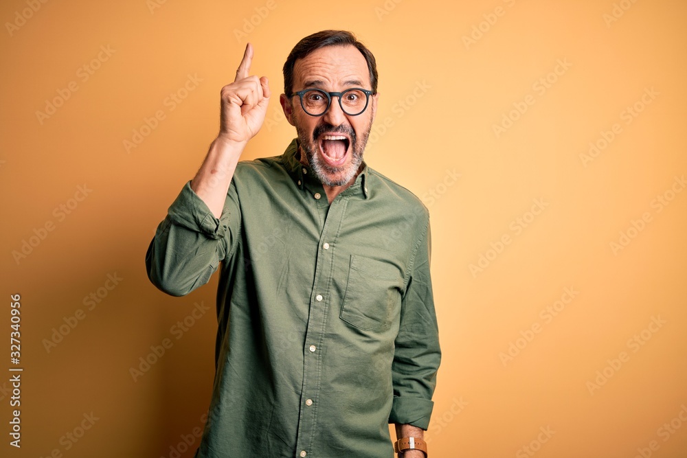 Middle age hoary man wearing casual green shirt and glasses over isolated yellow background pointing finger up with successful idea. Exited and happy. Number one. Middle age hoary man wearing casual green shirt and glasses over isolated yellow background pointing finger up with successful idea. Exited and happy. Number one.