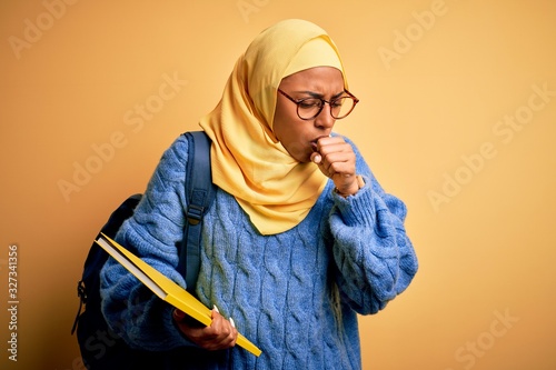 Bild auf Leinwand Young African American student woman wearing muslim hijab and backpack holding book feeling unwell and coughing as symptom for cold or bronchitis