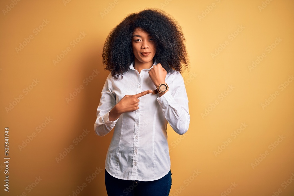 Young beautiful african american elegant woman with afro hair standing over yellow background In hurry pointing to watch time, impatience, looking at the camera with relaxed expression Young beautiful african american elegant woman with afro hair standing over yellow background In hurry pointing to watch time, impatience, looking at the camera with relaxed expression
