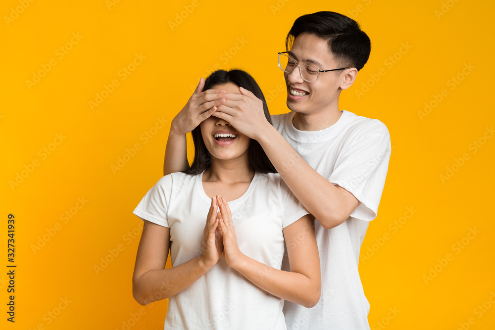 Asian man standing behind his girlfriend and closing her eyes