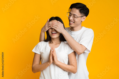 Asian man standing behind his girlfriend and closing her eyes