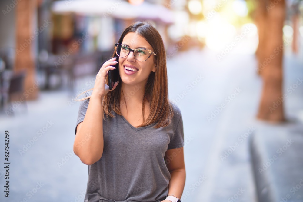 Young beautiful woman smiling happy and confident. Standing with smile on face talking by the smartphone at town street