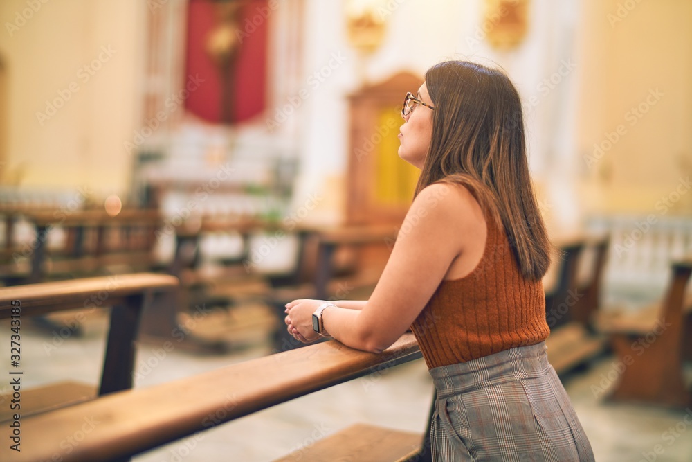 Young beautiful woman praying on her knees in a bench at church Young beautiful woman praying on her knees in a bench at church