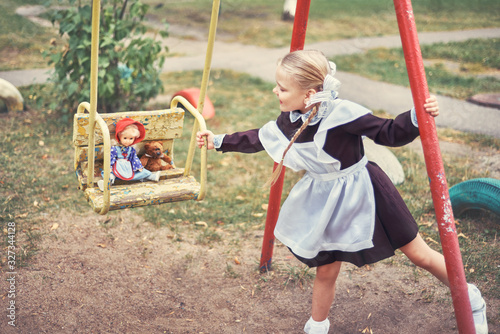 cute little girl schoolgirl in uniform rides children's toys on swing.