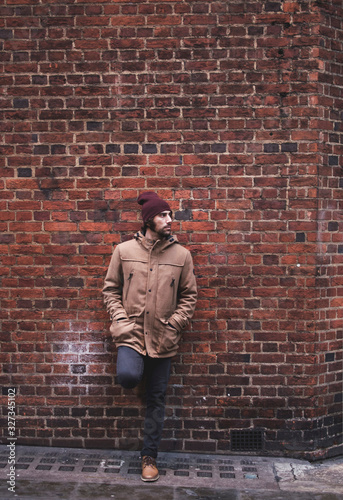 фотографія Young man with hat and warm clothes leaning against brick wall looking sideways