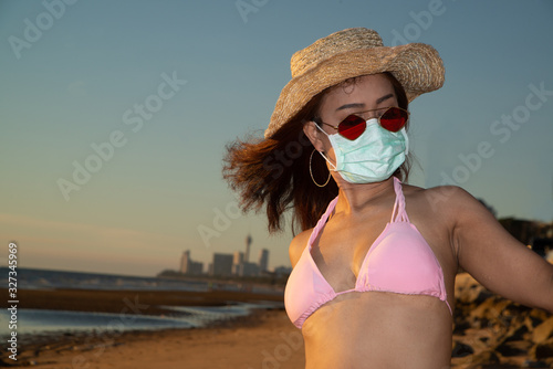 An senior Asian woman dressed in a pink swimsuit wears a straw hat and has a nose mask. Lantan Virus COVID-19 and PM2.5 protection. photo