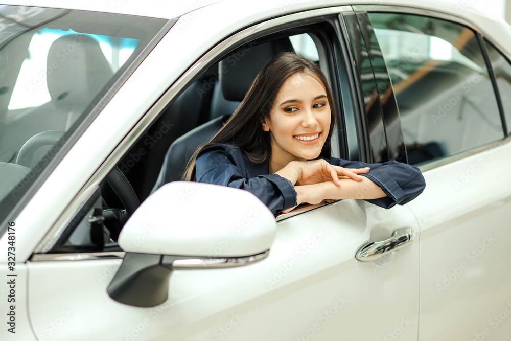 positive caucasian lady sitting inside of her new car in dealership. young beautiful woman happy after buying representative car