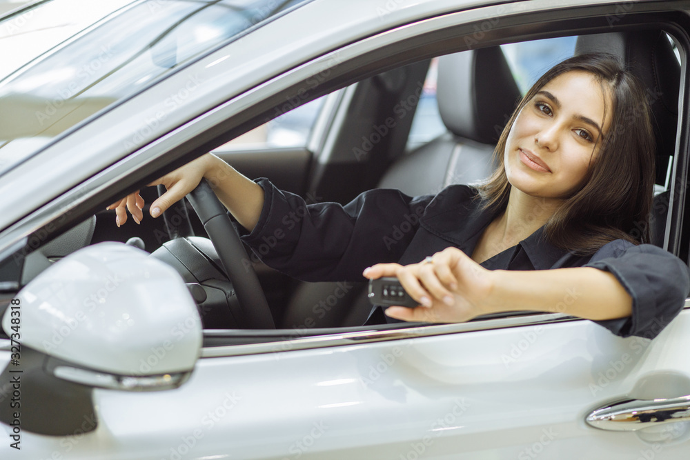 attractive beautiful caucasian woman came to buy new automobile in representative dealership. happy lady sit inside of car and enjoy it, holding keys from car