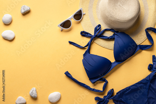 straw hat, women's bikini swimsuit and sun glasses on a yellow background. Summer fashion flat lay. horizontal image. copy space.