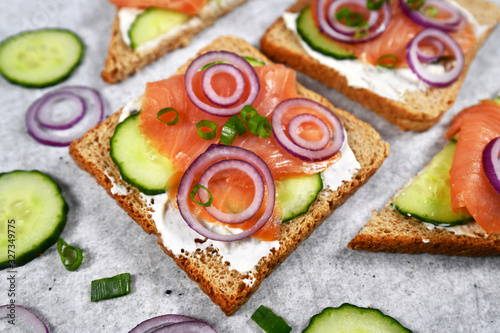 Slice of healthy wholegrain toast bread topped with smoked salmon fish, red onions and spring onions and cucumber on horseradish 