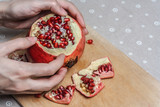 Female hand showing a cut pomegranate fruit. Woman hands peel red fresh pomegranate on wooden cutting board