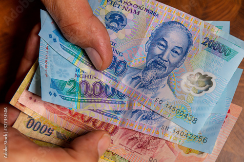 Male hand holds a fan of  Vietnames Dong banknote, the currency of Vietnam.  Close up Polymer Money of Vietnam. 20000 Dong or VND in male hand. In front a portrait of Ho Chi Minh. Plastic banknotes