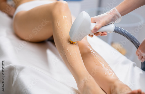 close-up of young caucasian slender woman getting laser epilation in beauty salon. hair removal from legs with the use of special apparatus photo