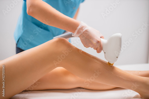 close-up photo of young woman getting laser hair removal procedure on her legs in modern clinic. cosmetology and spa, skin care concept photo