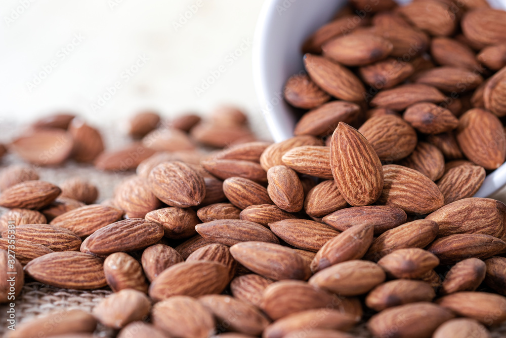 Closeup of almonds nut in white bowl were poured on sacks. Almond nut is popular and high protein nutrition. Closeup of almonds nut in white bowl were poured on sacks. Almond nut is popular and high protein nutrition.