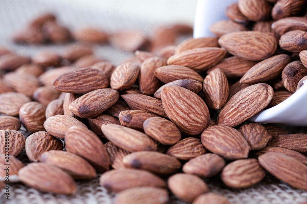 Closeup of almonds nut in white bowl were poured on sacks. Almond nut is popular and high protein nutrition. Closeup of almonds nut in white bowl were poured on sacks. Almond nut is popular and high protein nutrition.