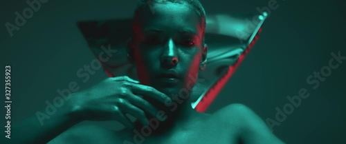 Sensual seductive model girl slowly moves or dances in neon light, red and blue lighting in studio, fashion photo shoot, night club noir atmosphere. Cute face of young woman with trendy shine makeup
