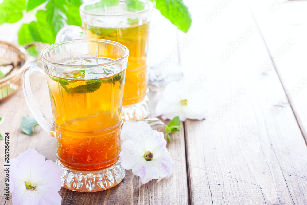 Black iced tea with lemon and mint in glass cups on a wooden table, horizontal, copy space