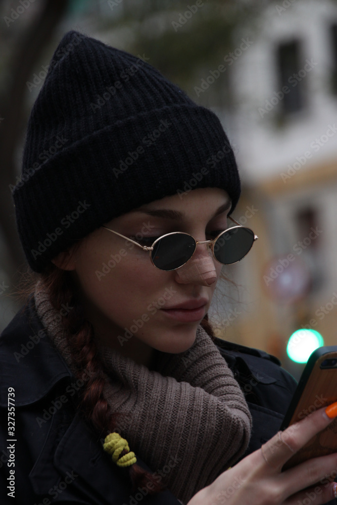Young woman with black hat and sunglasses looking her smartphone in the street Young woman with black hat and sunglasses looking her smartphone in the street