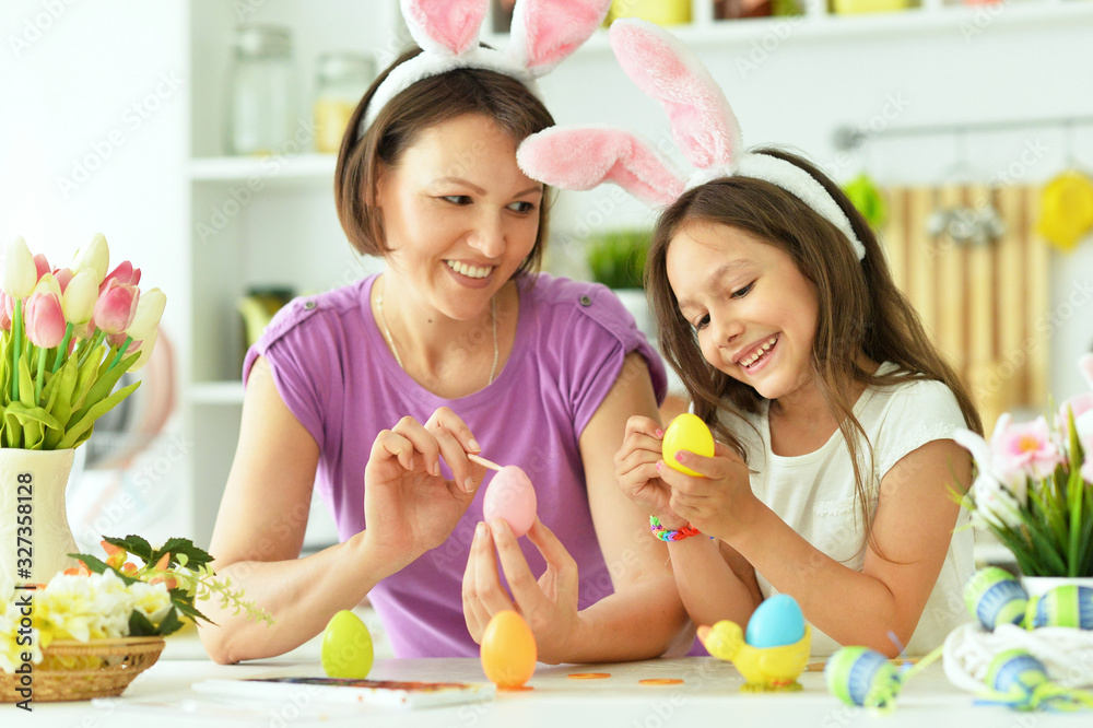 Mother with daughter wearing rabbit ears decorating Easter eggs at home Mother with daughter wearing rabbit ears decorating Easter eggs at home